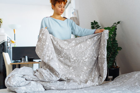 young woman makes bed and folds blanket neatly