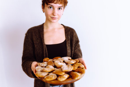 young woman holding gingerbread cookies on wooden round boardの写真素材