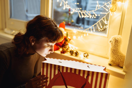 Young girl with gift box near christmas tree at homeの写真素材