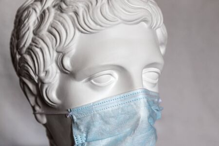 The head of an antique sculpture in a medical face mask. Coronavirus pandemic concept.