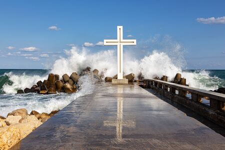 Waves are breaking into thousands of splashes on a pier with a cross mounted on it. The picture was taken in Bulgaria at the resort of Saints Constantine and Helena.の写真素材