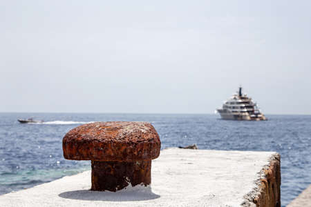Close-up of a brown bollard (harbor mooring post) on the pier against the backdrop of the receding yacht, the sea and the gray-blue sky. Selective focus.の写真素材