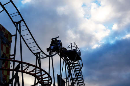 Amusement park: A bottom view of a booth moving at a height along curved rails. Silhouettes of people against the background of the dramatic sky.の写真素材