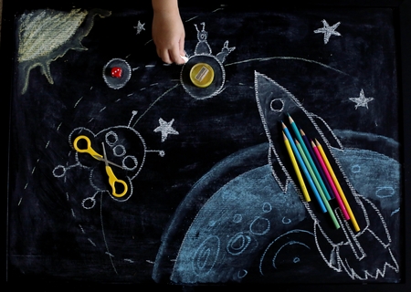 Space chalkboard background with rocket, planets and stars made from pencils, sharpener and scissors. View from above with drawing kid hands.の写真素材
