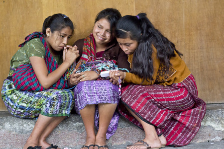 ANTIGUA, GUATEMALA - SEPTEMBER 16, 2013: Three poor girls share a cell phone on the streets of Antigua. September 16, 2013 in Antigua, Guatemalaのeditorial素材