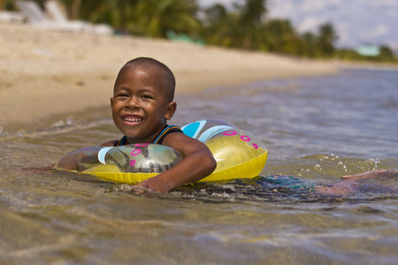 PLACENCIA, BELIZE - SEPTEMBER 22, 2013: Kid playing in the sea with his float. September 22, 2013 in Placencia, Belize. Belize is considered the 4th happiest country in the worldのeditorial素材