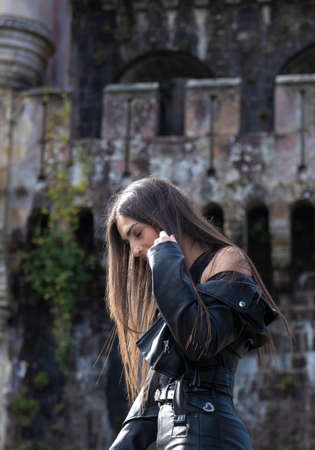portrait of pretty young brunette woman dressed in a leather jacket in front of an old castleの写真素材