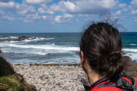 brunette woman trekking looking out to sea in a rocky cove de