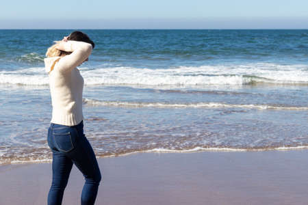 woman walking along the beach shore in jeans and wool sweaterの写真素材