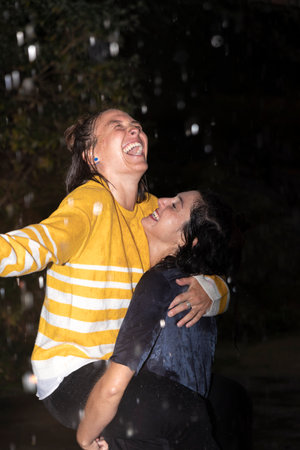 young lesbian couple hugging laughing and having fun in the rainの写真素材