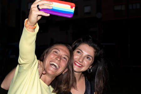 lesbian couple taking a selfie with a mobile with the gay flag