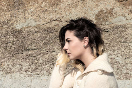 portrait of a woman in profile with a woolen sweater and a rock wall behind
