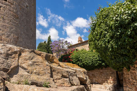 stone alley with a tree and a tower in the medieval village of pals on the costa bravaの写真素材