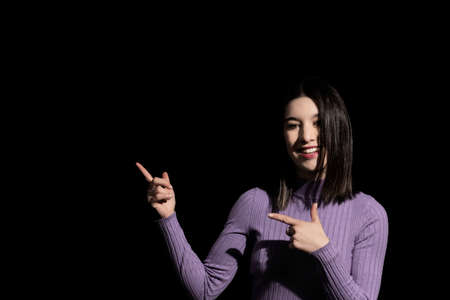 brunette woman on black background pointing to her rightの写真素材
