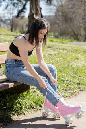 brunette woman tying pink roller skates on a park bench