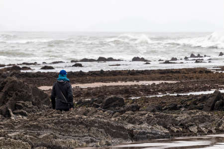 man walking between rocks accompanied by his dog on the seashore