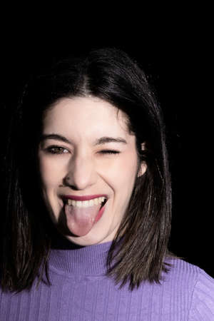 brunette woman winking and sticking out her tongue on black background