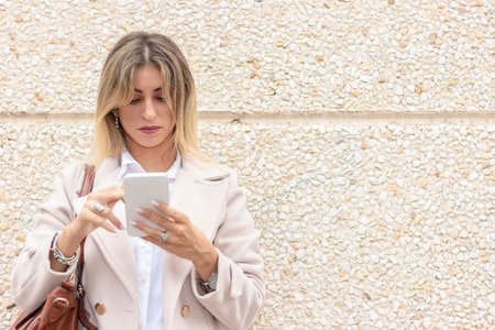 modern young business woman leaning on a wall looking at mobile