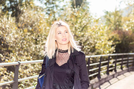 Confident blonde walking on a bridge one sunny day dressed in black