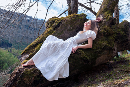 woman lying in the forest on a large log in a white dressの写真素材