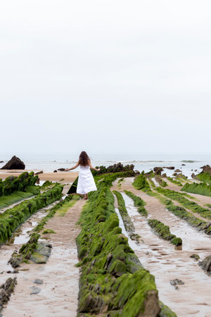 young brunette woman in a white dress walking among the rocks on the beachの写真素材