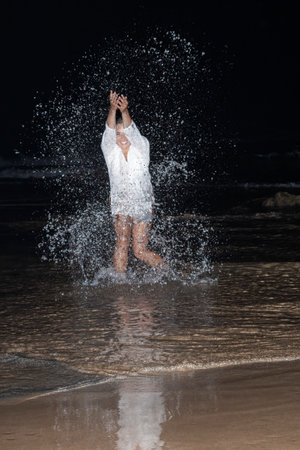 Beautiful model girl making splashes in the sea and laughing at night. Beautiful Woman enjoying the Waves of the Ocean. tropical vacationの写真素材