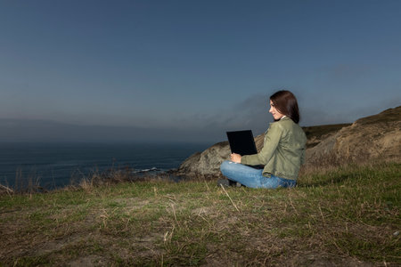 Young woman, the freelancer sitting on a high cliff over the sea and works remotelyの写真素材
