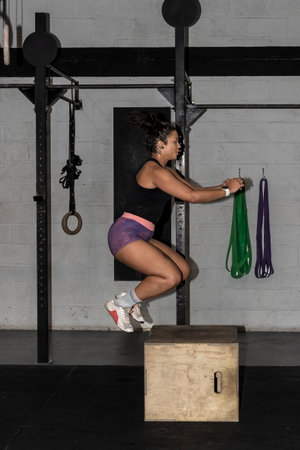 young latin woman jumping on a box as part of exercise routine. Fitness woman doing box jumps at...