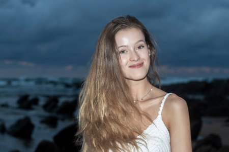 beautiful blonde woman smiling at camera on the beach at sunsetの写真素材