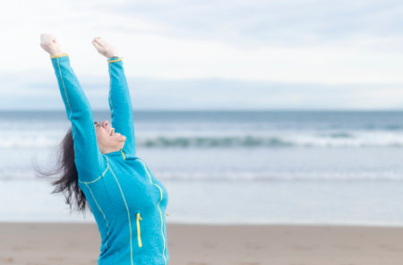 happy woman raising arms on the beach in winterの写真素材