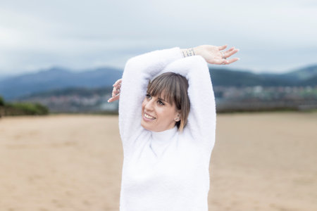 beautiful woman in a white sweater holding her head happily on the beachの写真素材