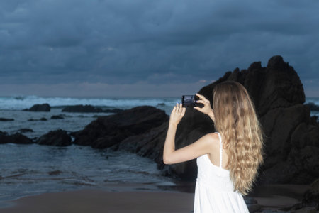 Woman hands holding mobile phone at sunset. Young woman taking photos with her cell phone in a...
