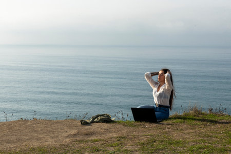 Digital nomad lifestyle concept with adult woman sit down on the ground with scenic view of beach and ocean inbackground - work with technology internet laptop computer in alternative free officeの写真素材