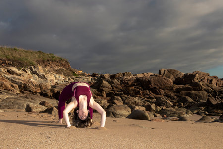 girl does yoga on the ocean.Yoga on the beach, flexible sports model performs gymnastic elements