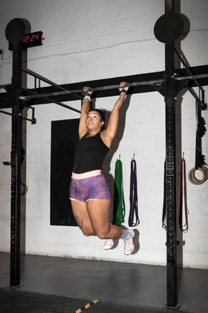 Young woman doing exercises in the gym. athlete woman doing abs exercises on horizontal bar Practicing calisthenics in the gym Shot of a strong latin woman in sportswear.の写真素材