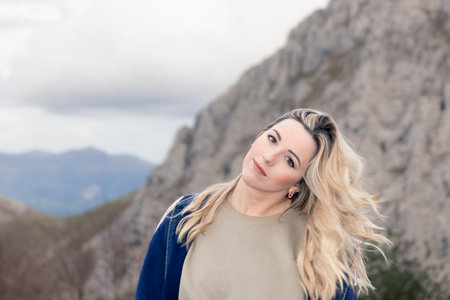 Blonde Beauty Amidst the Mountains: Captivating Gaze Towards the Cameraの写真素材