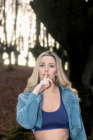 Captivating Beauty of a Blonde Woman Gesturing Silence in the Enchanting Forestの写真素材