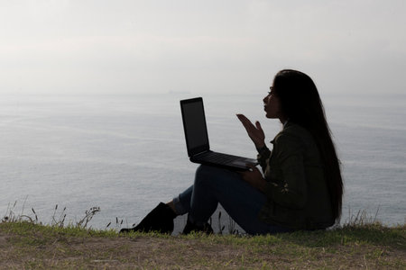 Paradise: Beautiful Woman Engaged in a Virtual Meeting Amidst Beachside Tranquilityの写真素材