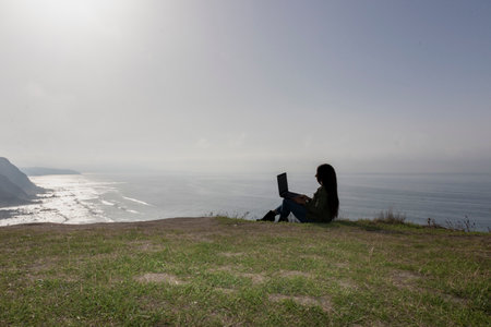 Stylish Woman Conducting a Video Conference Against an Ocean Backdropの写真素材