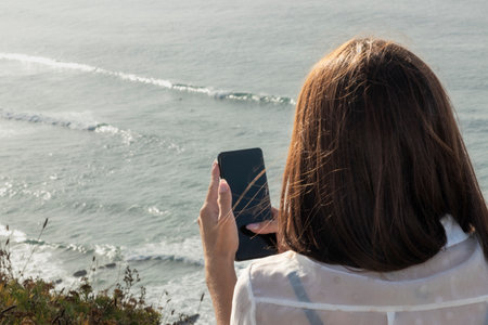 Brunette Woman Lost in Her Phone's Glow, Absorbed by the Seasideの素材