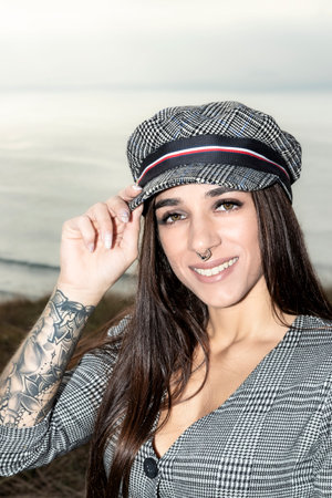Youthful Urban Elegance: Confident Brunette in a Short Dress and Hat, Flaunting Expressive Tattoosの素材