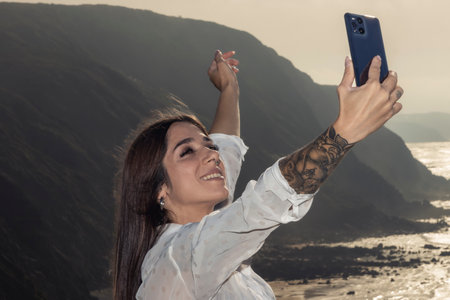 Brunette Woman Captures the Stunning Cliffside View with Confidence and Tattooed Styleの素材
