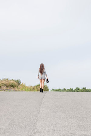 Confident Brunette Woman Strides Away on a Road, Flaunting Short Plaid Dressの写真素材