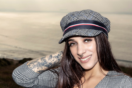 Trendy Brunette with Tattooed Arm Wearing Gray Plaid Dress and Capの写真素材