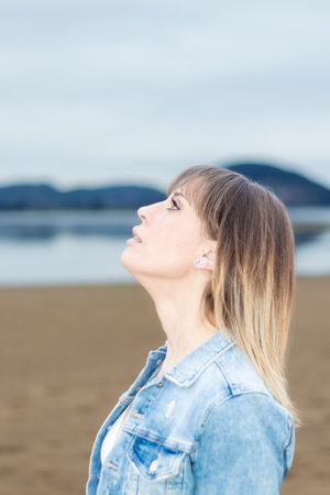 Dreamy Beachside Beauty: Woman's Profile in a Denim Jacket, Lost in Thought, at Ocean's Edgeの写真素材