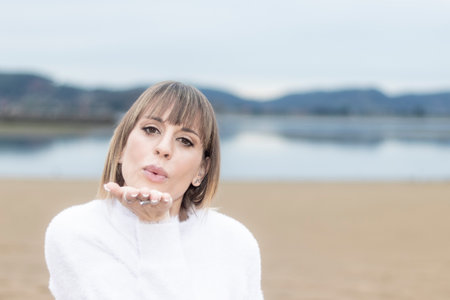Beachside Elegance: Beautiful Woman in a White Sweater Blows a Kiss in the Serene Coastal Breezeの写真素材