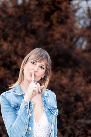 woman in a denim jacket and a white lace top making the silence gestureの写真素材
