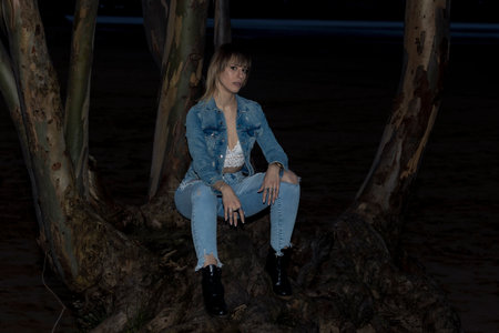 Nighttime Serenity: Person in Denim Sitting on a Tree Trunk by the Beachの写真素材