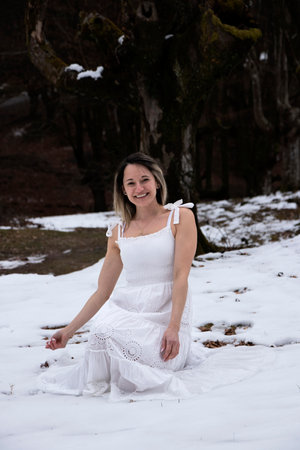 woman in a white dress is sitting in the snow with trees in the backgroundの写真素材