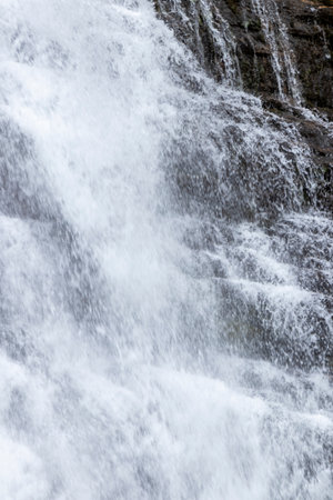 close-up photo of a frothy, white waterfall cascading down a dark, jagged cliff faceの写真素材